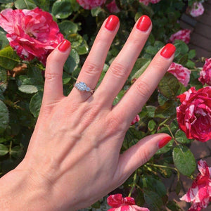 Woman wears three-stone engagement ring by flowers