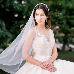 Bride looks to the side as she wears veil, headpiece, diamond earrings and necklace