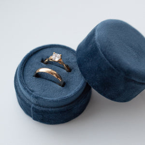 A yellow gold engagement ring and wedding band is set into a blue velour ring box