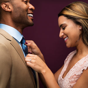 Woman smiles as she adjusts mans tie and wears engagement ring